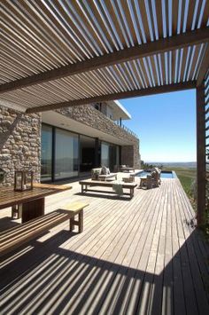 a wooden deck with benches and tables next to a large stone building that overlooks the water