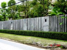 a fence that is next to a street with trees and bushes on the other side