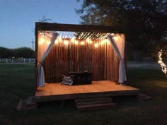 a small wooden structure with string lights on the top and curtains hanging from it's sides