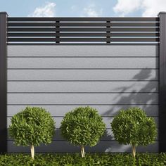 three small trees are in front of a gray wall with horizontal slats on it