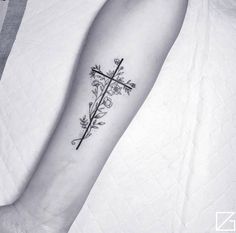 a cross and flowers tattoo on the left forearm, with an arrow in the middle