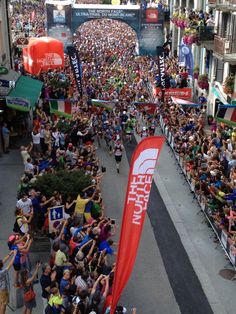 a large group of people walking down a street next to tall buildings with banners on them