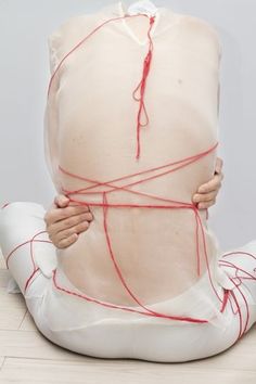 a woman sitting on the floor with her back wrapped in red string