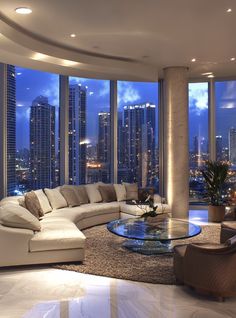 a living room filled with lots of furniture and tall buildings in the background at night