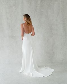 the back of a woman in a white wedding dress, standing against a gray wall