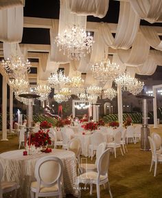 a banquet hall with tables and chairs covered in white drapes, chandeliers and flowers