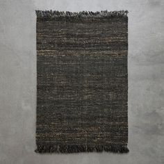 a black and brown rug with fringes on the bottom, against a gray wall