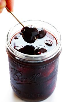 a hand holding a spoon over a jar filled with liquid and sauce on a white surface