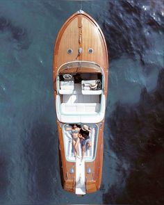 two people are sitting on the back of a boat in the water, looking down