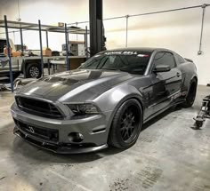 a silver mustang parked in a garage next to other cars and equipment on the floor