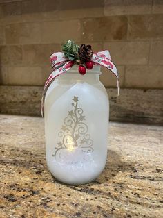 a white glass jar with a christmas tree on the lid and a red ribbon around it