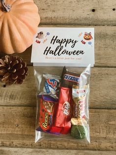 an assortment of candy in a bag with a happy halloween sign on the top and a pine cone next to it