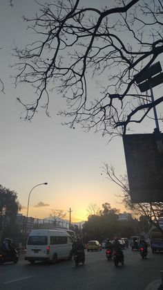 the sun is setting on a busy street with cars and motorcyclists driving down it