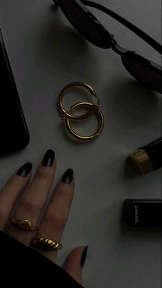 a woman's hand with black and gold nail polish next to various accessories on a table