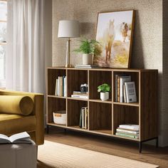 a living room with a couch, book shelf and lamp on the side table in front of a window