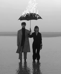 two people standing in the water holding an umbrella with flames coming out of it,