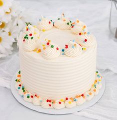 a cake with white frosting and colorful sprinkles on the top is sitting on a plate next to flowers