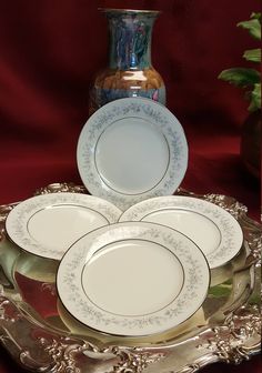 four white plates on a silver platter with a vase in the background and red cloth