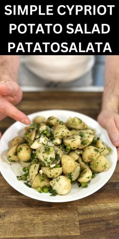 a white plate topped with potato salad on top of a wooden table next to two hands