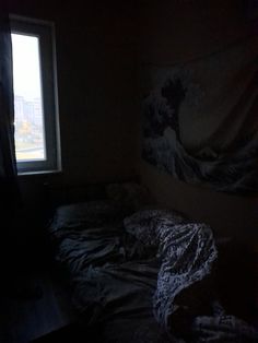 an unmade bed sitting next to a window in a dark room