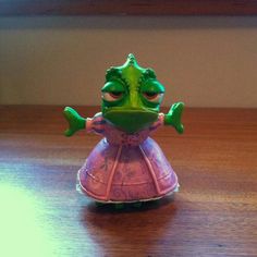 a toy frog in a pink dress sitting on a table