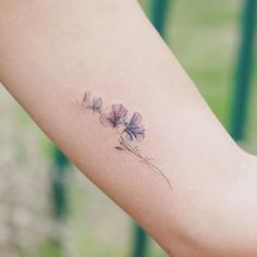 a woman's arm with a small purple flower tattoo on the left inner arm