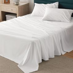 a bed with white sheets and pillows on top of it next to a night stand