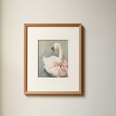 a white swan with a pink bow on it's head in a wooden frame