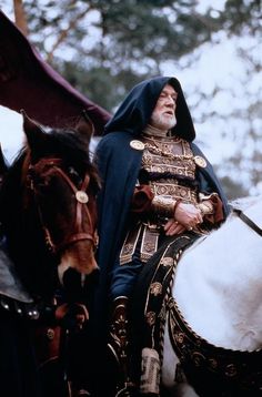 an old man sitting on top of a white horse next to another person in costume