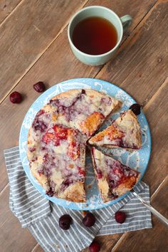 a blue plate topped with a piece of cake next to a cup of tea and cherries