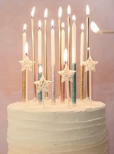 a birthday cake with white frosting and gold stars on top, lit by candles