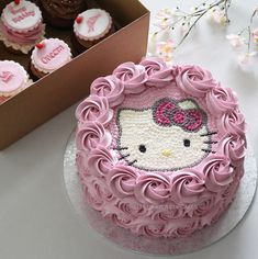 a hello kitty birthday cake with pink frosting and cupcakes in the background