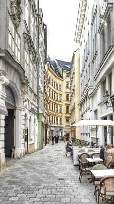 people are sitting at tables in the middle of an alleyway with buildings on both sides