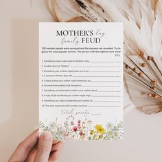 someone holding up a mother's day card with flowers and feathers in the background