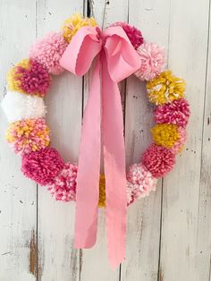 a wreath with pink, yellow and white pom - poms