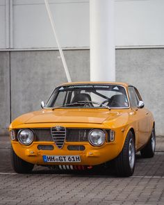 an old yellow car parked in front of a building