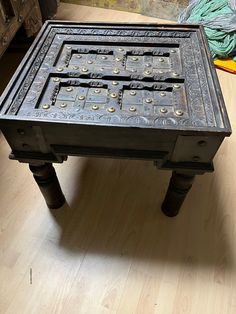 an old wooden table with metal rivets and knobs on the top, sitting on a hard wood floor