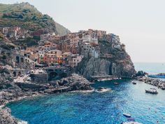 boats are in the water near a small village on a rocky cliff above the ocean