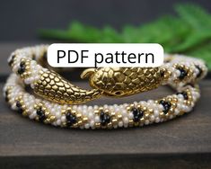 three bracelets with gold and white beads on top of a wooden table next to green leaves