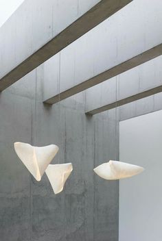 two white lamps hanging from the ceiling in a room with concrete walls and beams on either side