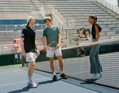 three men standing on a tennis court holding racquets and talking to each other