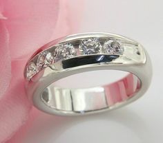 a wedding ring with three diamonds on it and a pink rose in the back ground