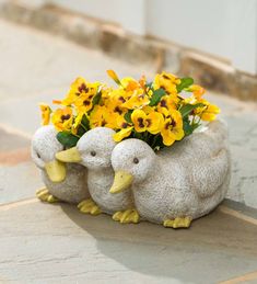 two ceramic ducks with yellow flowers in their beaks sitting on the ground next to each other