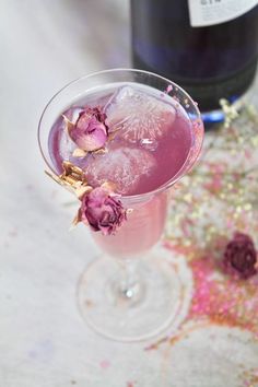 a glass filled with pink liquid and flowers next to a bottle of wine on a table