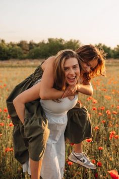 two young women are playing in a field full of flowers and one is hugging the other