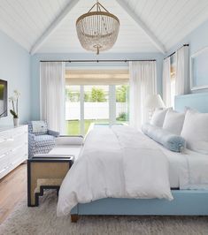 a bedroom with blue walls, white bedding and a chandelier hanging from the ceiling