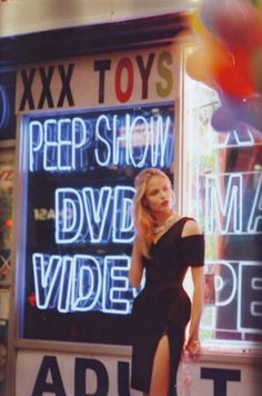 a woman standing in front of a store window with neon signs on it's side