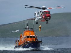 a helicopter flying over a boat in the water with another boat below it and two men standing on the side of the boat