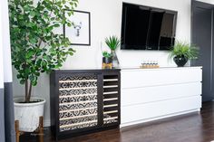 a tv mounted on the wall above a dresser next to a potted plant in a living room