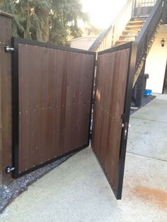 an open wooden gate on the side of a house with stairs in the back ground